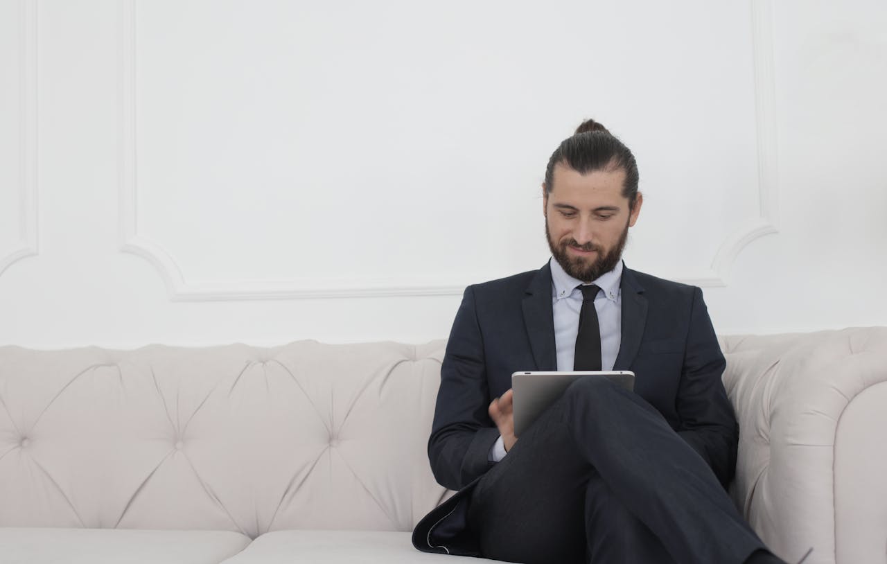 services-01 A businessman in a suit sitting on a sofa using a tablet, smiling.